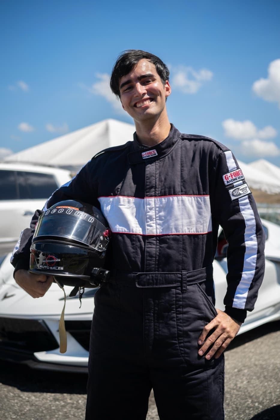 Oliver Infante con traje de competencia, sosteniendo el casco frente a un Corvette en el circuito.