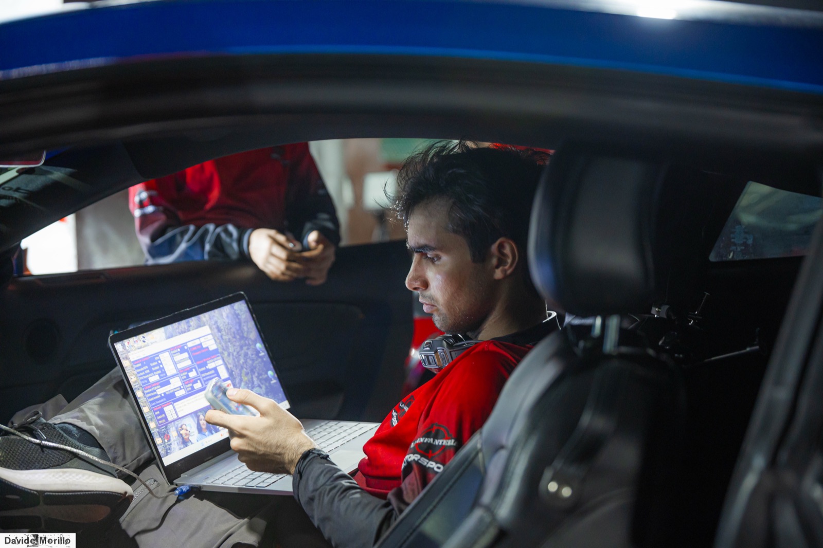 Oliver Infante analizando datos de telemetría en una laptop, sentado dentro del auto de carreras en el paddock.
